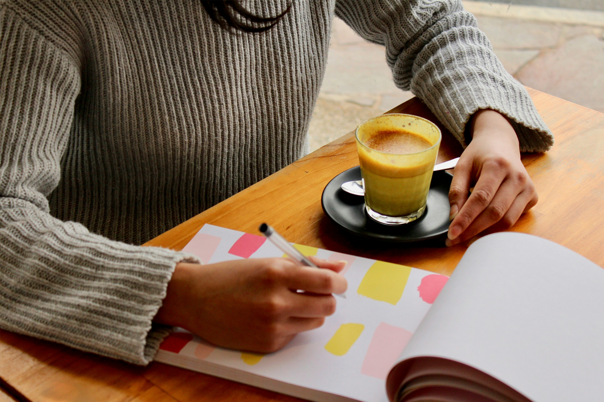 Person holding pen, taking notes on a notepad, with some coffee on table